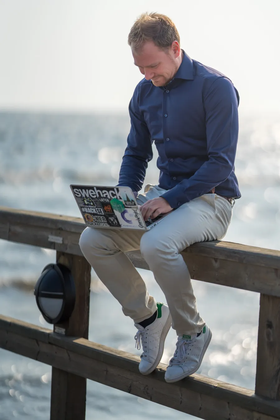 David Jacoby on a railing by the sea, laptop open